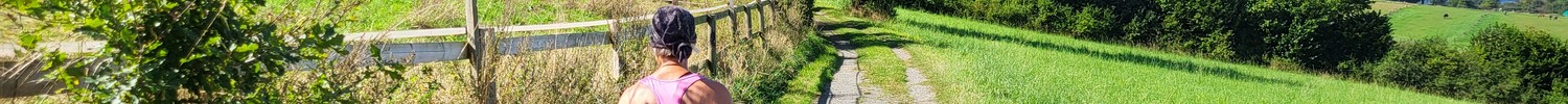 Wanderin auf Feldweg zwischen Weiden, Wiesen und Wald