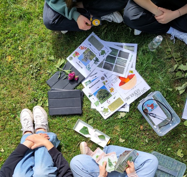 Bildungsmaterialien zwischen Personen auf einer Wiese liegend Bildungsmaterialien zwischen Personen auf einer Wiese liegend